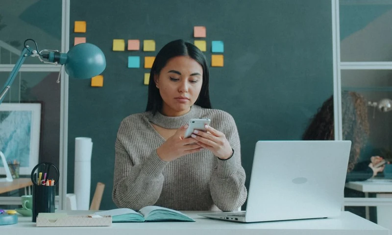 Mujer revisando su correo en el celular en su escritorio de trabajo