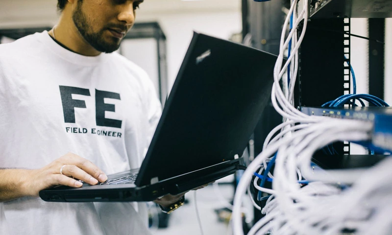 Técnico revisando un servidor con su laptop junto a un rack de red